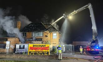 A firefighter on an aerial ladder platform spraying water onto a smoking derelict building