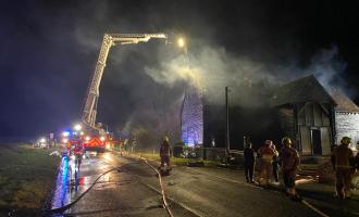 Large house at night, surrounded by smoke, a fire engine and firefighters