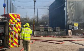 A firefighter next to a fire engine looking towards an industrial building