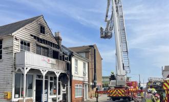 Wooden building (sailing club) damaged by fire with an aerial ladder platform in shot.