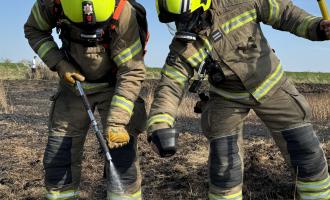 Two firefighters cooling a field after a wildfire