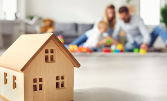 little toy wooden house in foreground and family in background