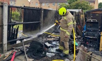 A firefighter spraying water on a scorched fence