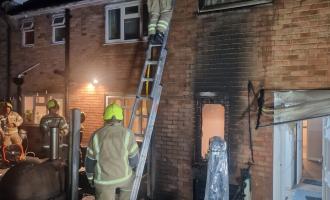 A firefighter on a ladder at the side of a scorched house