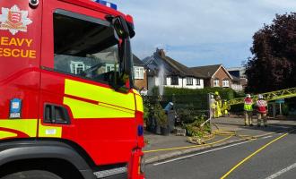 Firefighters walking towards the house affected by fire, with a fire engine in the foreground