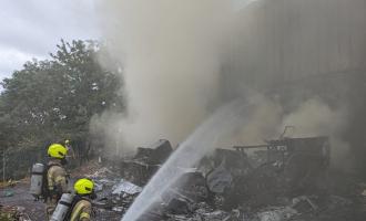 Firefighters spraying water on a burnt out camper van