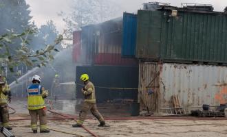 Firefighters in the foreground with smoke coming from containers in the background