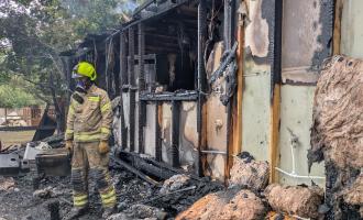 A firefighter outside a burnt-out wooden building