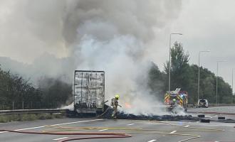 Firefighters spraying water on a smouldering pile of tyres next to a lorry
