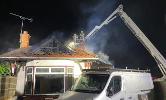 Firefighters on an aerial ladder platform with smoke coming out of a bungalow roof