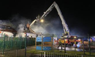 Firefighters on an aerial ladder platform with smoke coming out of the bungalow's roof