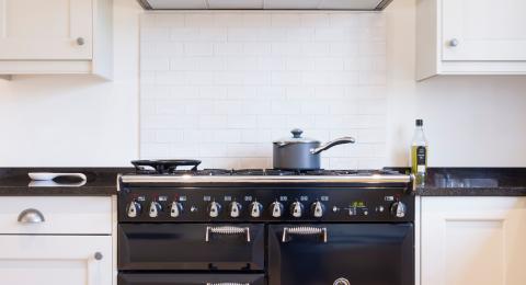 Close up of white kitchen with black worktop. Saucepan positioned on top of a black range cooker.