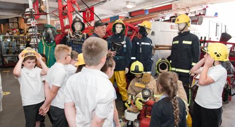 A museum volunteer gives a talk to some school children. They are trying on old fire helmets.