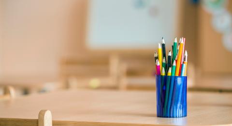 Blue pot filled with colouring pencils, set on wooden school desk