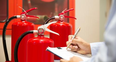 Three red fire extinguishers behind close up of man's arms holding a pen and a clipboard.