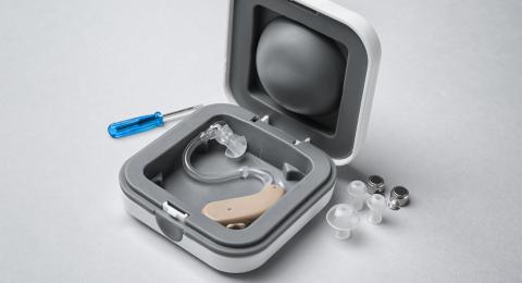 Hearing aid in silver case with small screwdriver on table