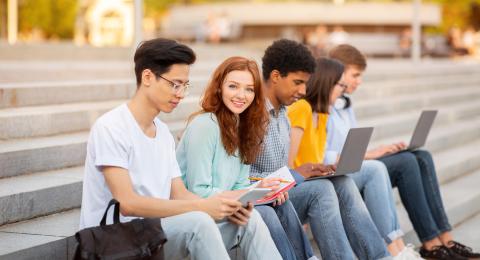 Group of five college friends sat on outdoor steps with laptops