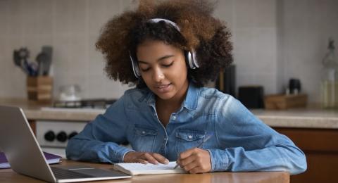 Teenage girl with headphones on sat at a laptop on a wooden table