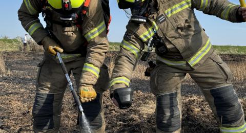 Two firefighters cooling a field after a wildfire