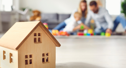 little toy wooden house in foreground and family in background