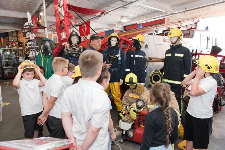 A museum volunteer gives a talk to some school children. They are trying on old fire helmets.