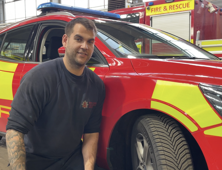 Tom Reed, an Engineer in our Fleet Workshops, in front of a red and yellow fire car. 