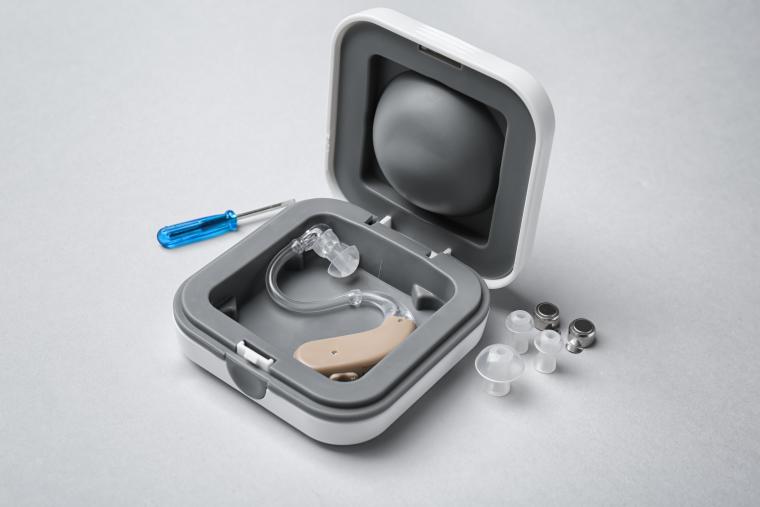Hearing aid in silver case with small screwdriver on table