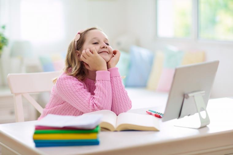 Girl, aged 9, wearing pink jumper sat at a laptop