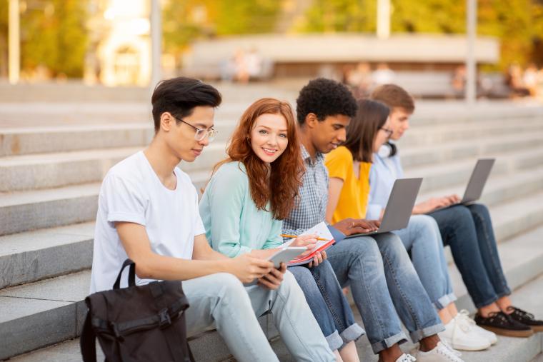 Group of five college friends sat on outdoor steps with laptops