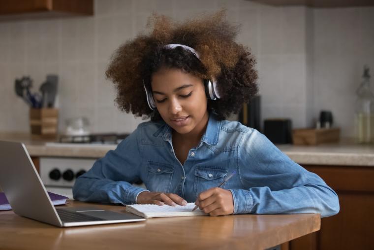 Teenage girl with headphones on sat at a laptop on a wooden table