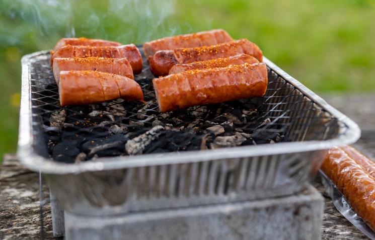 Sliced sausages on a disposable barbecue, set safely on a large concrete slab