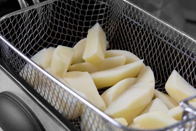 Close up of chipped potatoes in the basket of a deep fat fryer, ready for cooking