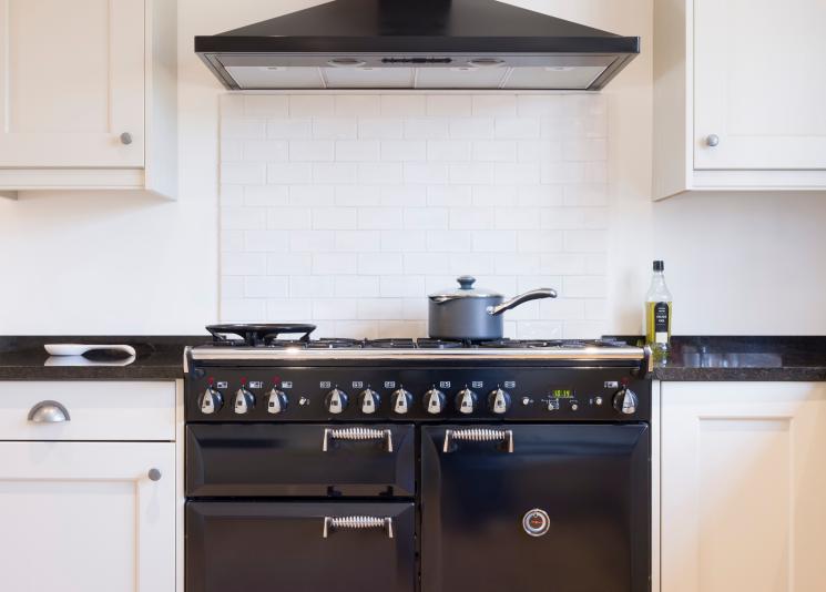 Close up of white kitchen with black worktop. Saucepan positioned on top of a black range cooker.