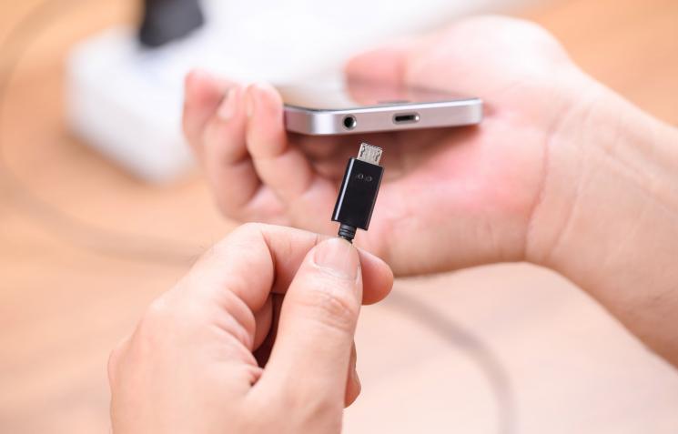 A hand holding a phone and the other hand placing a charger into the charging port