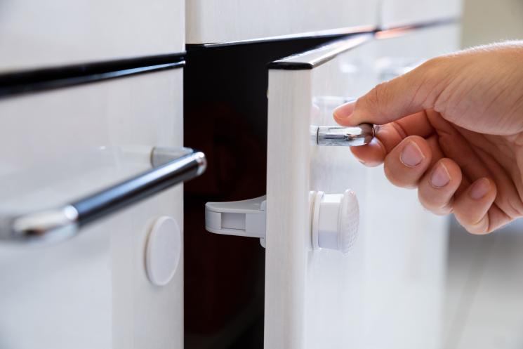 Hand opens white glossy cupboard door to reveal a child safety lock