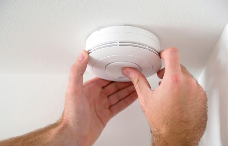 Men's hands testing smoke alarm on ceiling