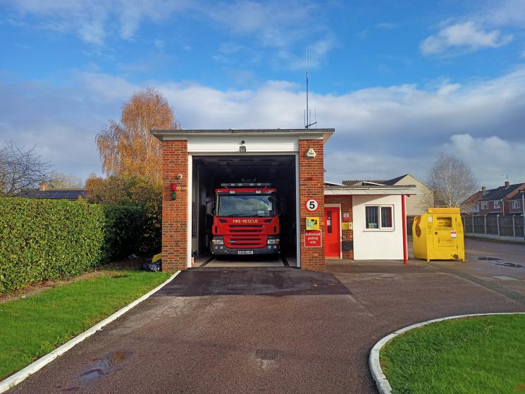 Small fire station building with one fire engine sitting inside a red bay door