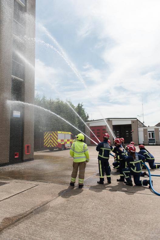 Group of Fire Break participants in PPE use hoses on practice tower on Fire Station forecourt