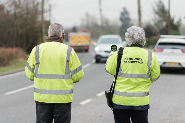 Two community speedwatch volunteersin high vis jackets checking speeds of passing cars