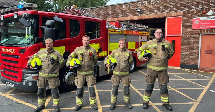 Four Firefighters outside their station with an appliance also in the background