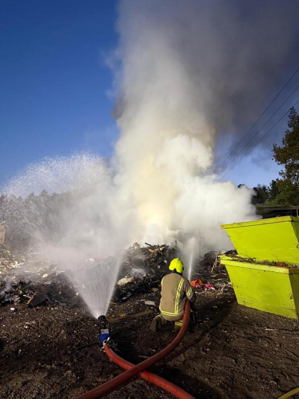 Firefighters spraying water on a pile of waste