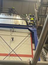 A firefighter climbs up a ladder to reach the top of the biomass boiler hopper, which is a square metal structure. 