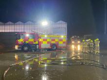 The side view of a fire engine and the front view of another fire engine in the dark in front of a plant nursery building. 