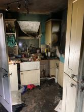 The front view of a kitchen that has been blackened from smoke and fire damage. You can see a space where the tumble dryer has been removed. 