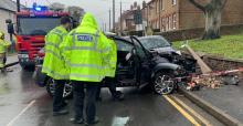 Police officers looking at a black car which has collided with a lamppost