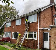 Two firefighters with a ladder using a hose to pour water onto a house fire