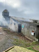 The outside of a barn with smoke coming out of the door.