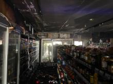 The inside of a shop, with lots of products on shelves, but everything is dark and smoke damaged following a fire. 
