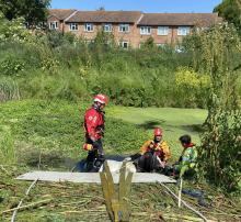 A hose stuck in water in a field. Three people surround it, attempting a rescue,