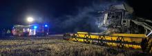 A fire engine and burnt out combine harvester in a scorched field